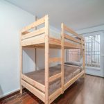 Neat bedroom with a wooden bunk bed and minimalist decor, featuring natural lighting.