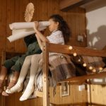 Two children playing with paper rolls on a decorated bunk bed in a wooden room.